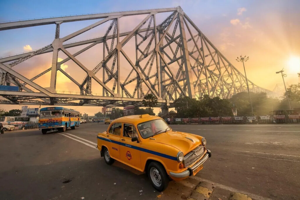 Kolkata`s iconic yellow taxi near Howrah Bridge, symbolizing metro-connected prime residential locations in 2025